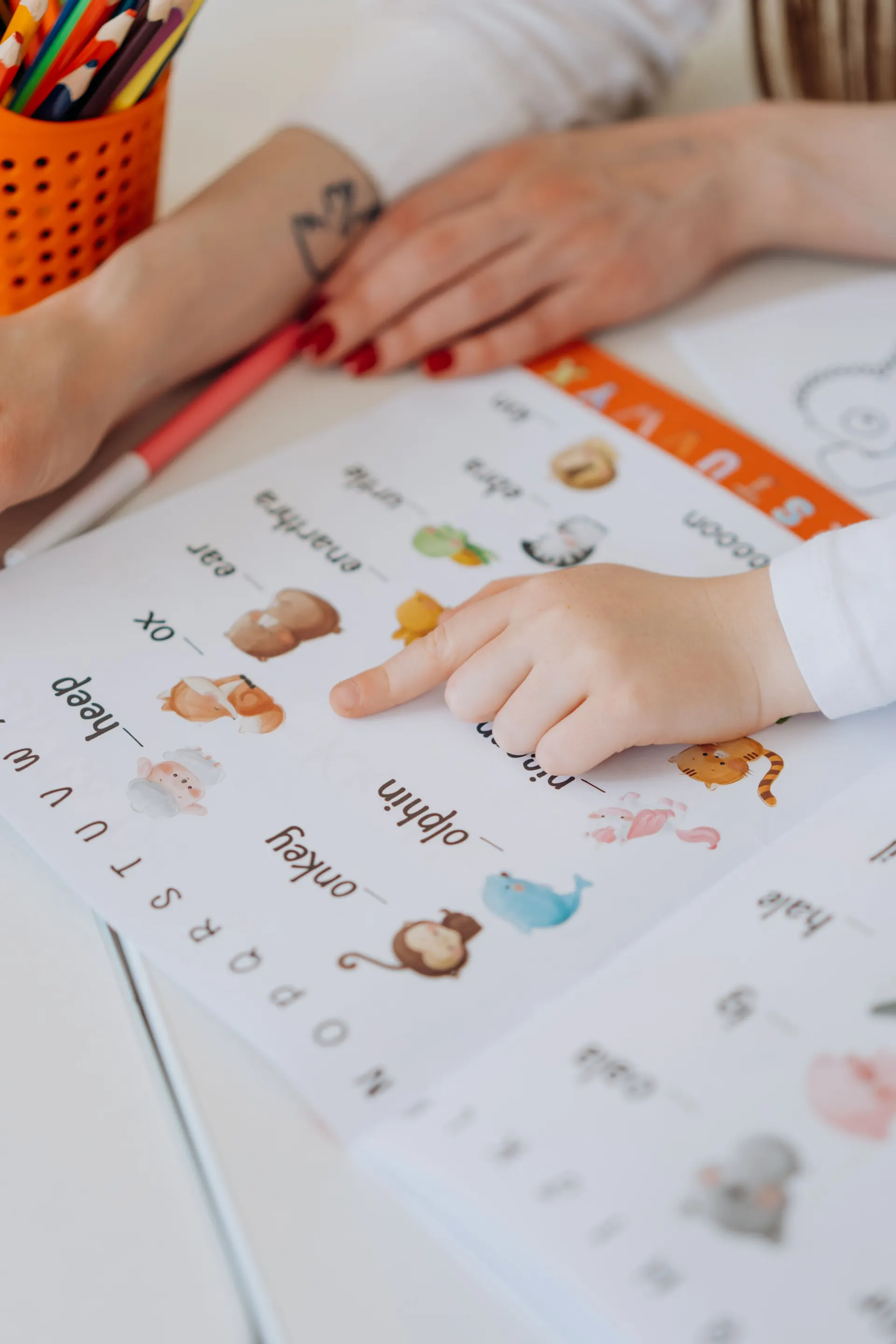 A child and adult practicing English vocabulary on a worksheet at a desk