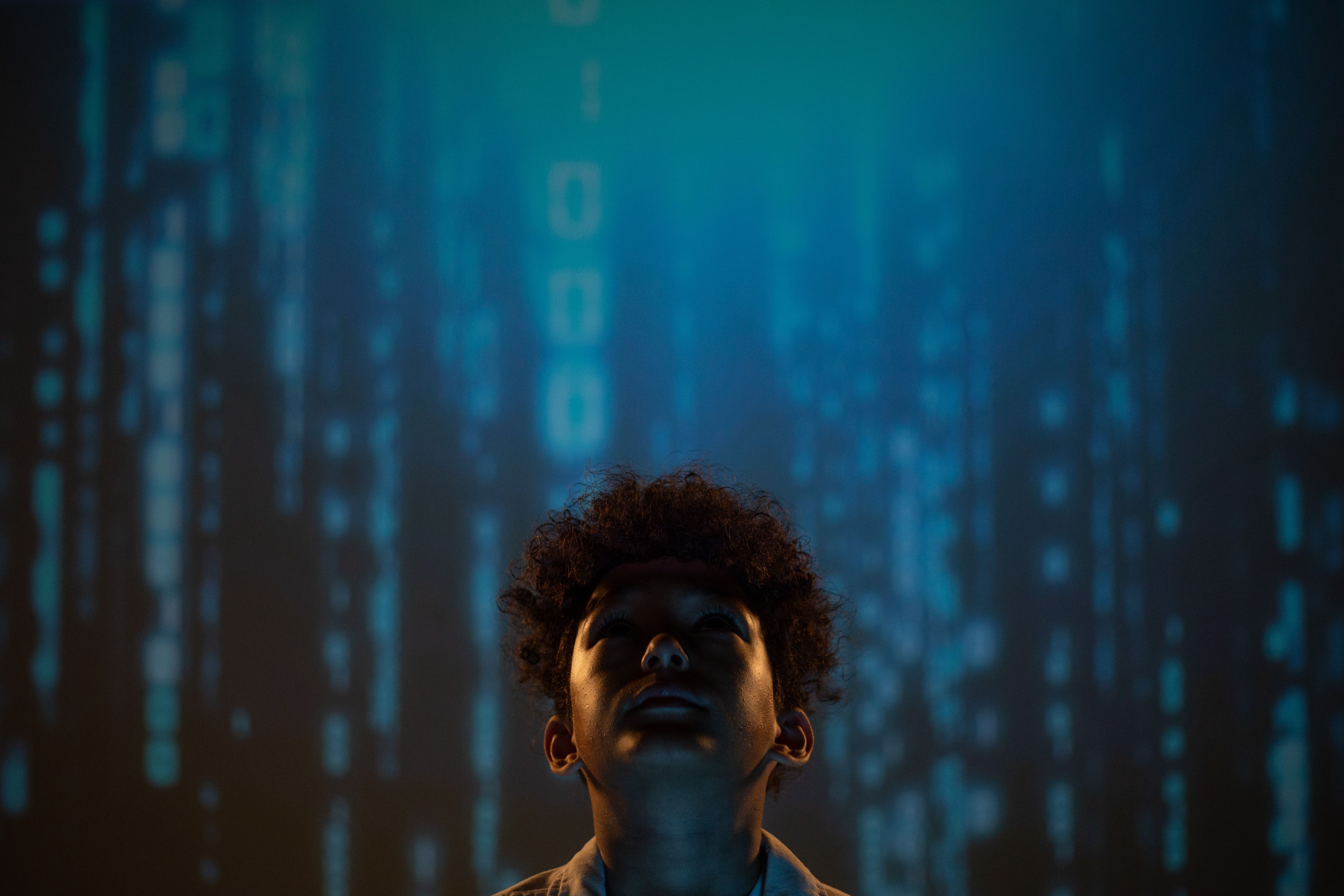 A young boy looking upward against a blue digital background, symbolizing a new generation in the age of AI