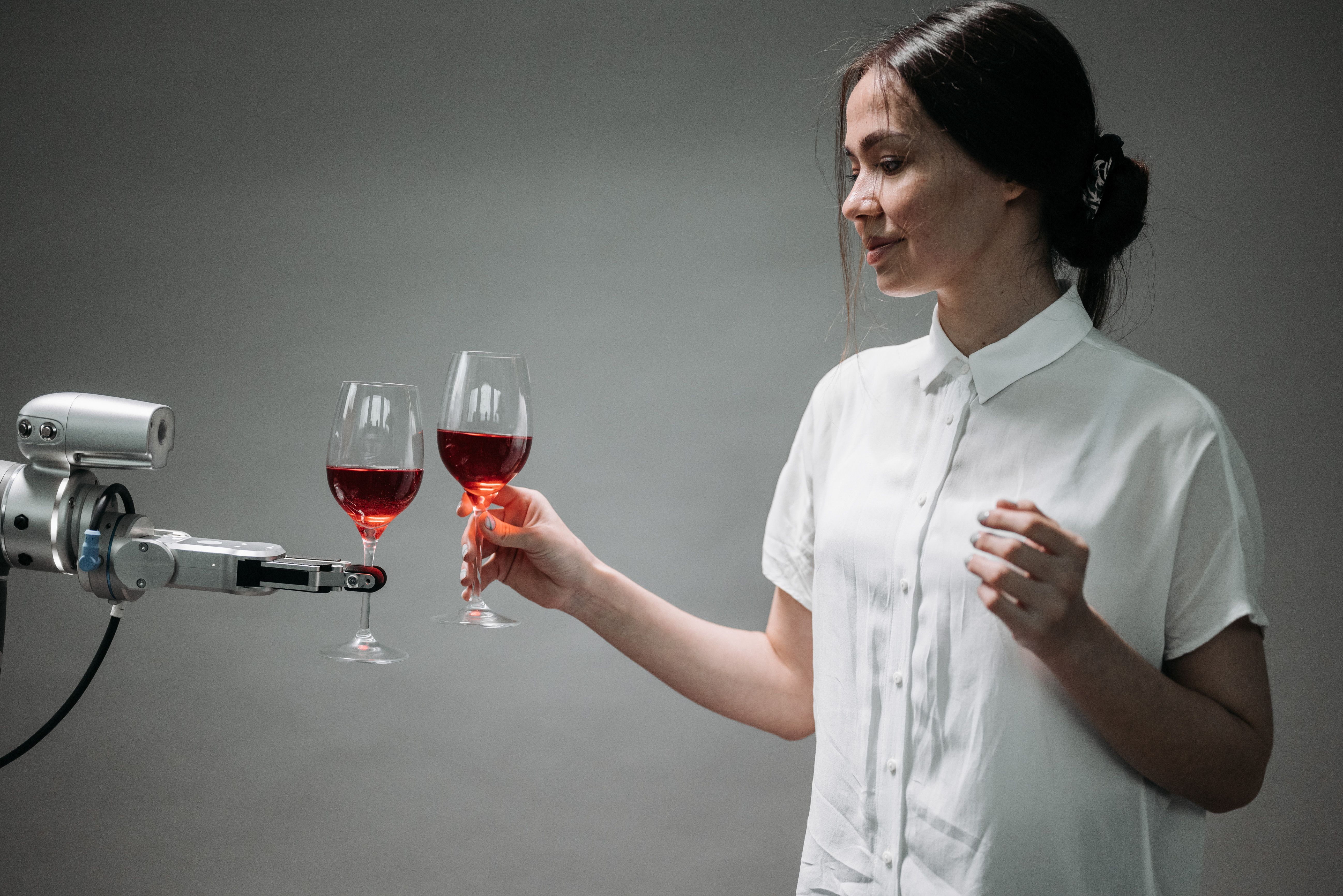 A woman and a robotic arm toasting with wine glasses, symbolizing human-AI collaboration